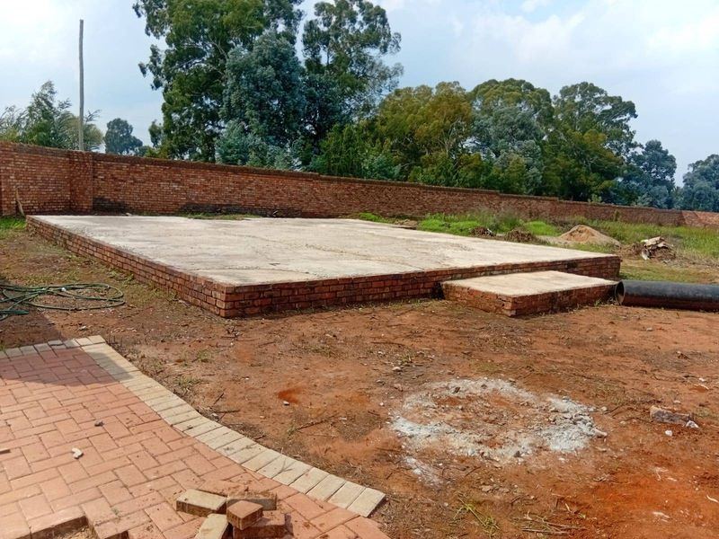 An outdoor area featuring a raised concrete slab foundation and a brick boundary wall, currently in an unfinished state.
