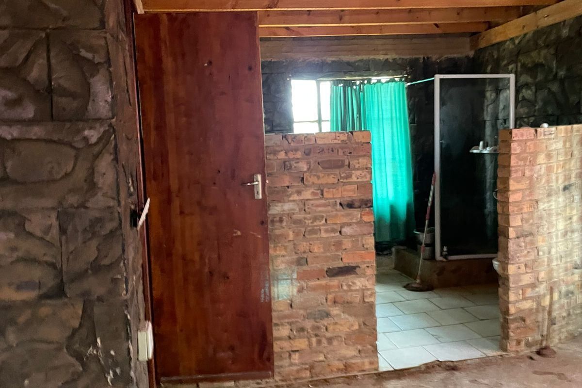 An unfinished bathroom space featuring exposed timber ceiling beams, stone wall cladding, and brick partition walls with a shower enclosure.