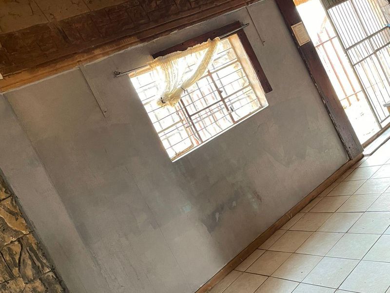 An empty living area featuring a traditional thatched roof with exposed timber beams, tiled flooring, and a stone feature wall.