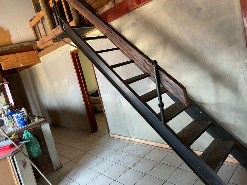 Open plan living area featuring a metal staircase leading to a mezzanine level, with tiled flooring and unfinished wall surfaces throughout.