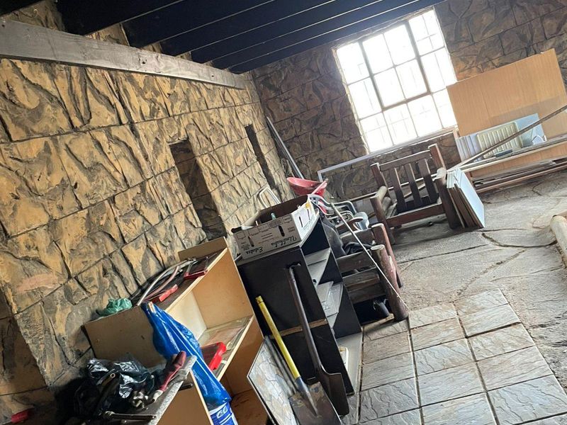 Utility space featuring stone-clad walls, exposed timber ceiling beams, and tiled flooring, offering potential for renovation or conversion into a functional living area.