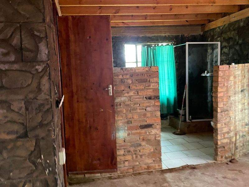 An unfinished bathroom space featuring exposed timber ceiling beams, stone wall cladding, and brick partition walls with a shower enclosure.
