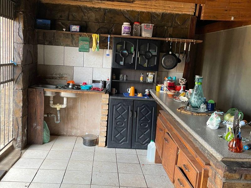 An outdoor patio area featuring a rustic stone wall, exposed timber beams, a thatch roof, and a built-in kitchenette with tiled flooring.