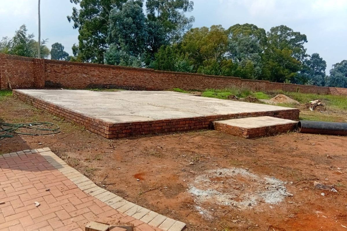 An outdoor area featuring a raised concrete slab foundation and a brick boundary wall, currently in an unfinished state.