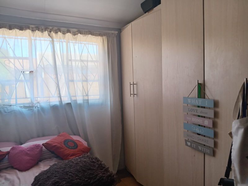 A bedroom featuring light-toned built-in wardrobes and a window fitted with security bars, providing functional storage and natural light.