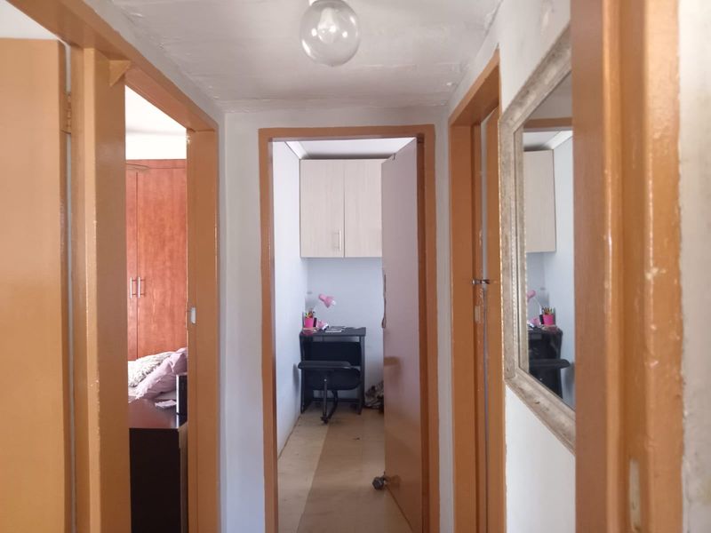 A narrow residential hallway featuring wooden door frames and access to adjacent rooms, including a small study area with built-in overhead cabinetry.