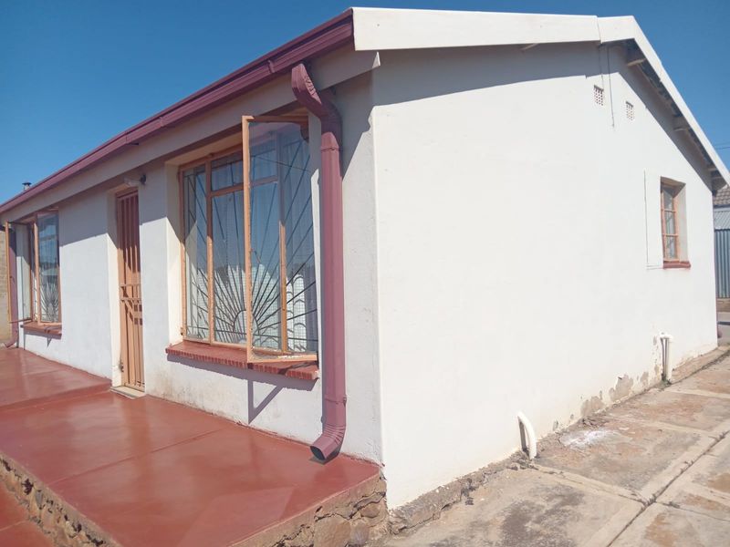 Front exterior view of a single-story house featuring painted walls, steel security gates, and a concrete patio area.