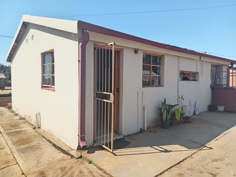Rear exterior view of the property featuring a concrete apron, metal security gate, and basic wall finishes with visible signs of wear.