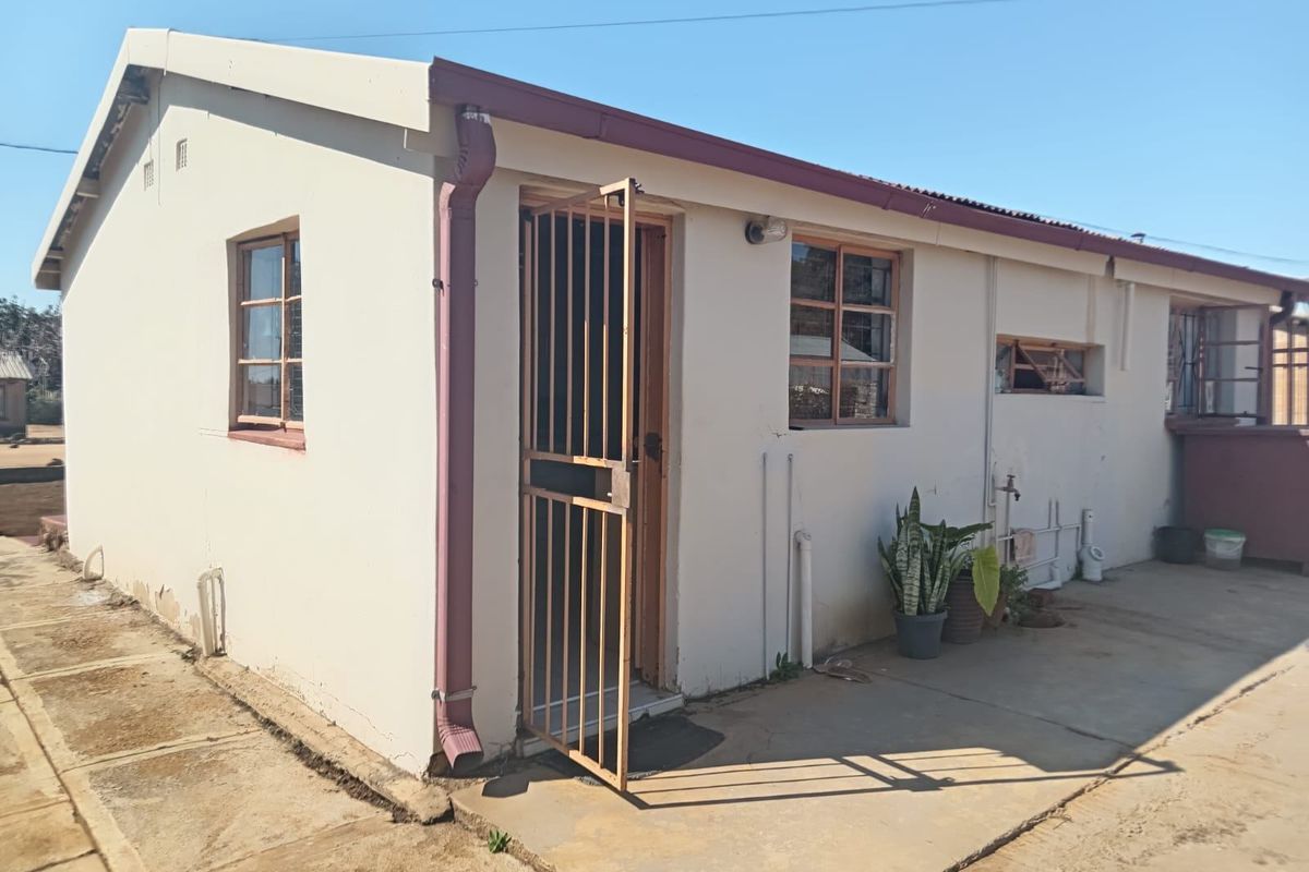 Rear exterior view of the property featuring a concrete apron, metal security gate, and basic wall finishes with visible signs of wear.