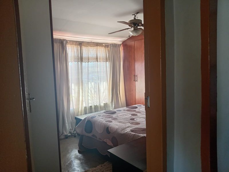 A bedroom featuring built-in wooden cupboards and a ceiling fan, viewed from the doorway.