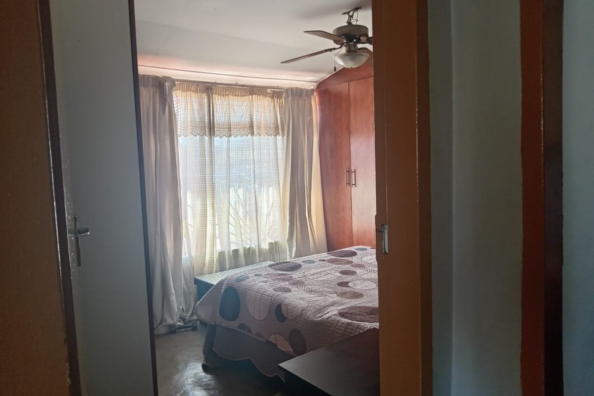 A bedroom featuring built-in wooden cupboards and a ceiling fan, viewed from the doorway.
