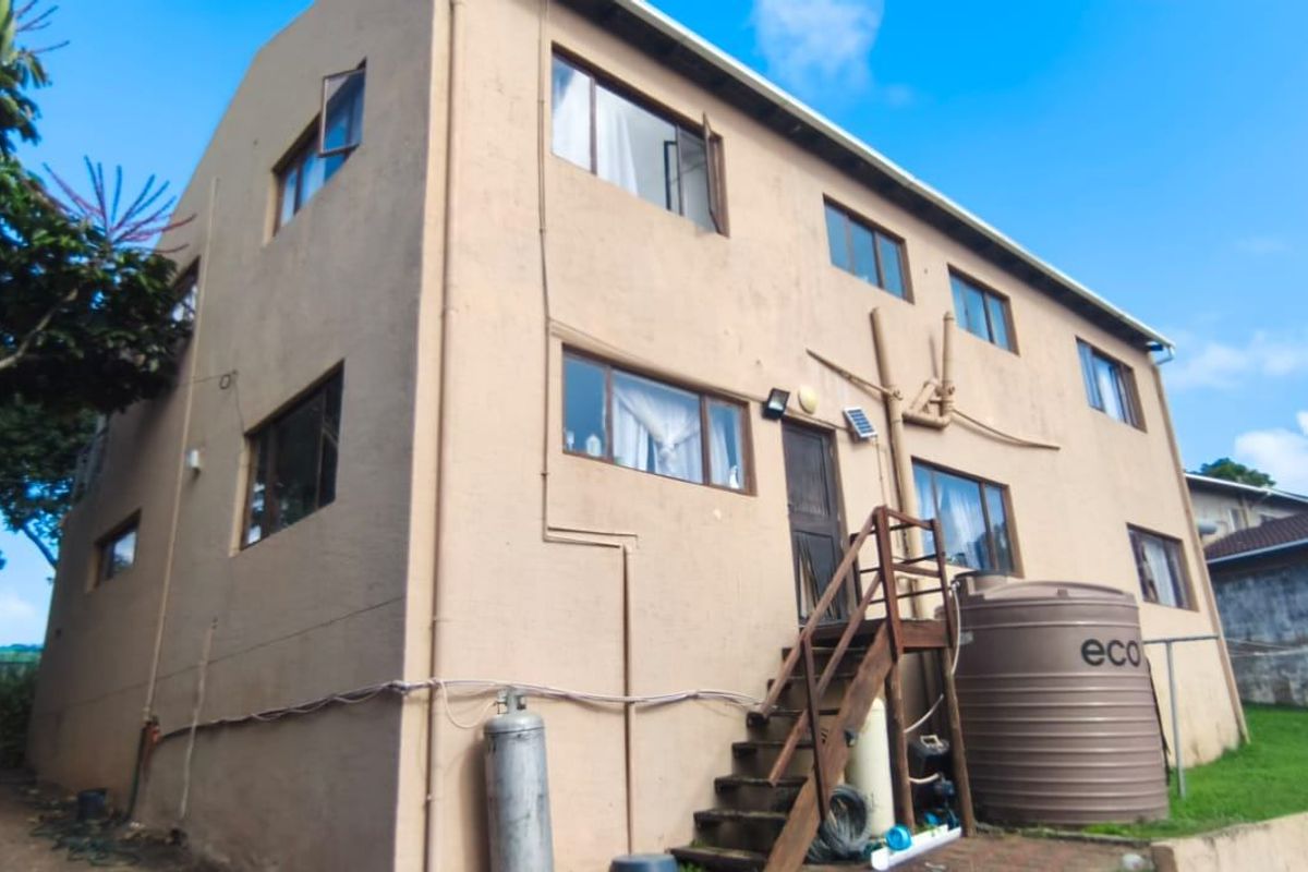 Rear view of a multi-story residential building featuring an external staircase, water storage tank, and gas cylinder installation.