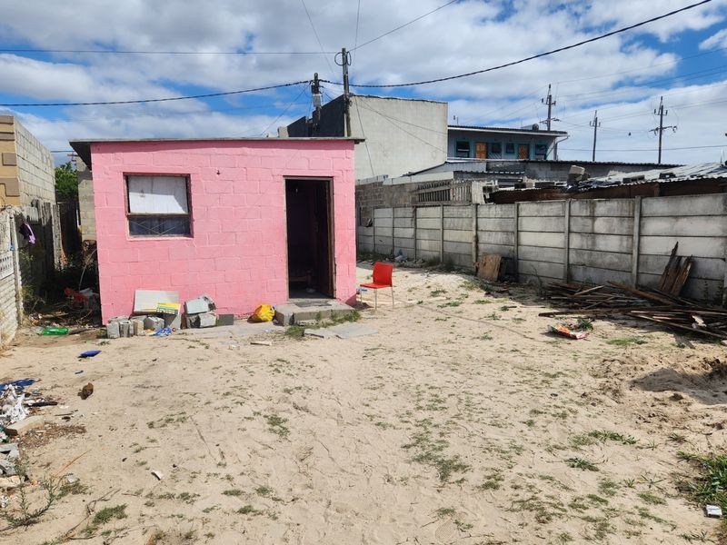 A detached pink concrete block structure situated in a large, unpaved rear yard enclosed by precast concrete boundary walls.