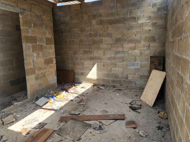 An unfinished room featuring exposed concrete block walls and a corrugated metal roof, currently in a shell state requiring significant completion and finishing.