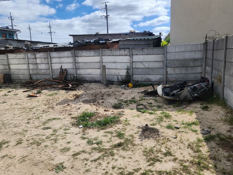 Rear outdoor area featuring a precast concrete boundary wall, currently requiring significant landscaping and debris removal to improve the property's exterior condition.