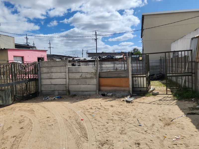 Rear exterior area featuring a precast concrete boundary wall with security gates and razor wire, set on an unpaved sandy surface.