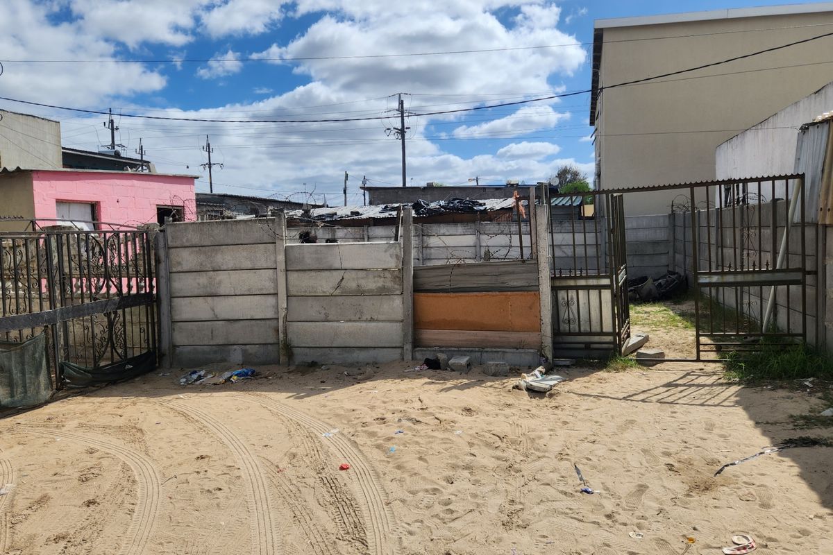 Rear exterior area featuring a precast concrete boundary wall with security gates and razor wire, set on an unpaved sandy surface.