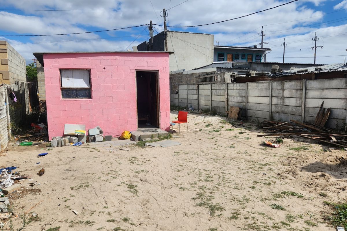 A detached pink concrete block structure situated in a large, unpaved rear yard enclosed by precast concrete boundary walls.