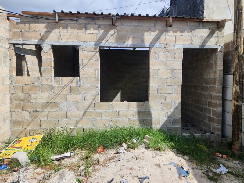 An unfinished residential structure featuring exposed concrete block walls and basic roof framing, requiring significant completion work.