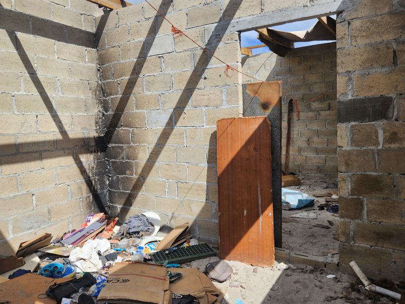 An unfinished interior space featuring exposed concrete block walls and roof framing, showing significant signs of fire damage and debris.