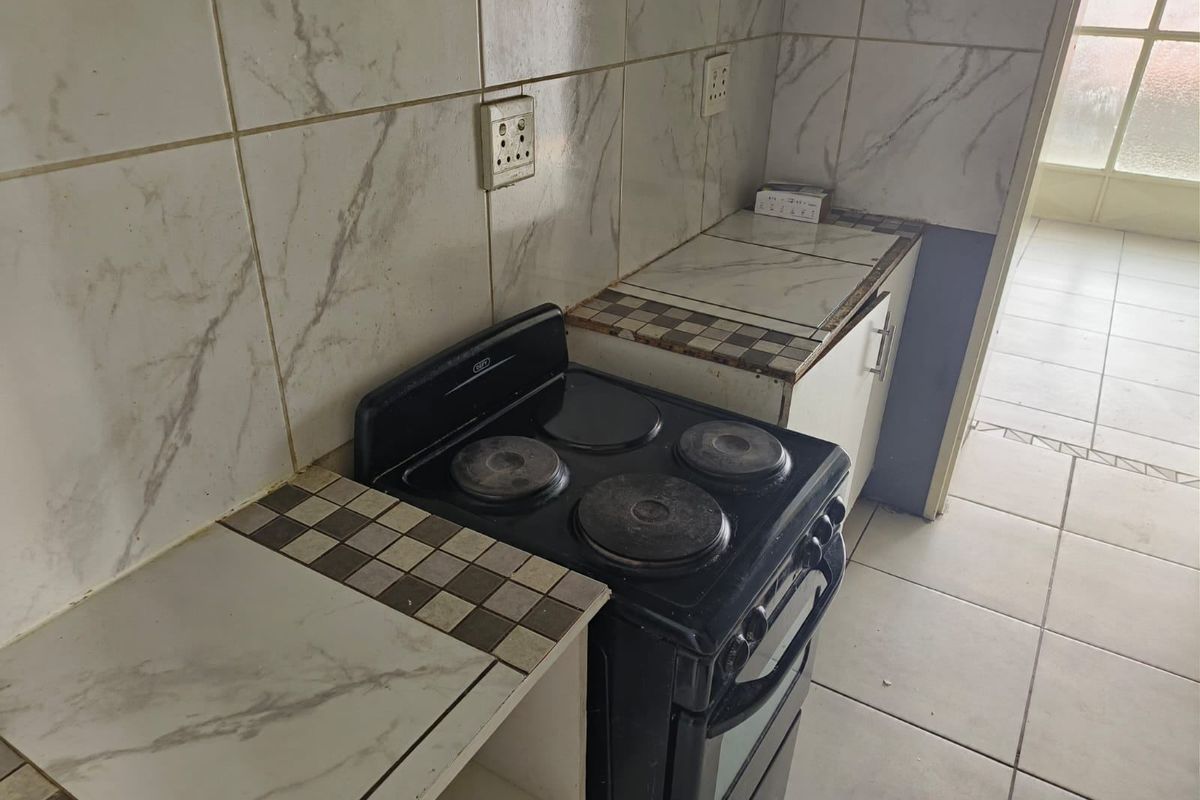 A compact kitchen area featuring a tiled backsplash, built-in cabinetry, and a freestanding electric stove, requiring cosmetic updates to modernize the space.