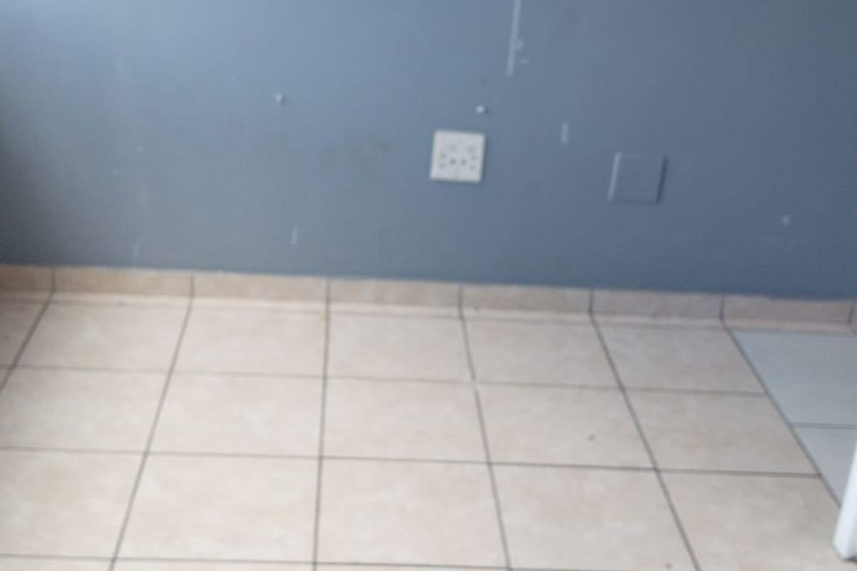An empty bedroom featuring neutral tiled flooring and blue painted walls with visible surface wear.