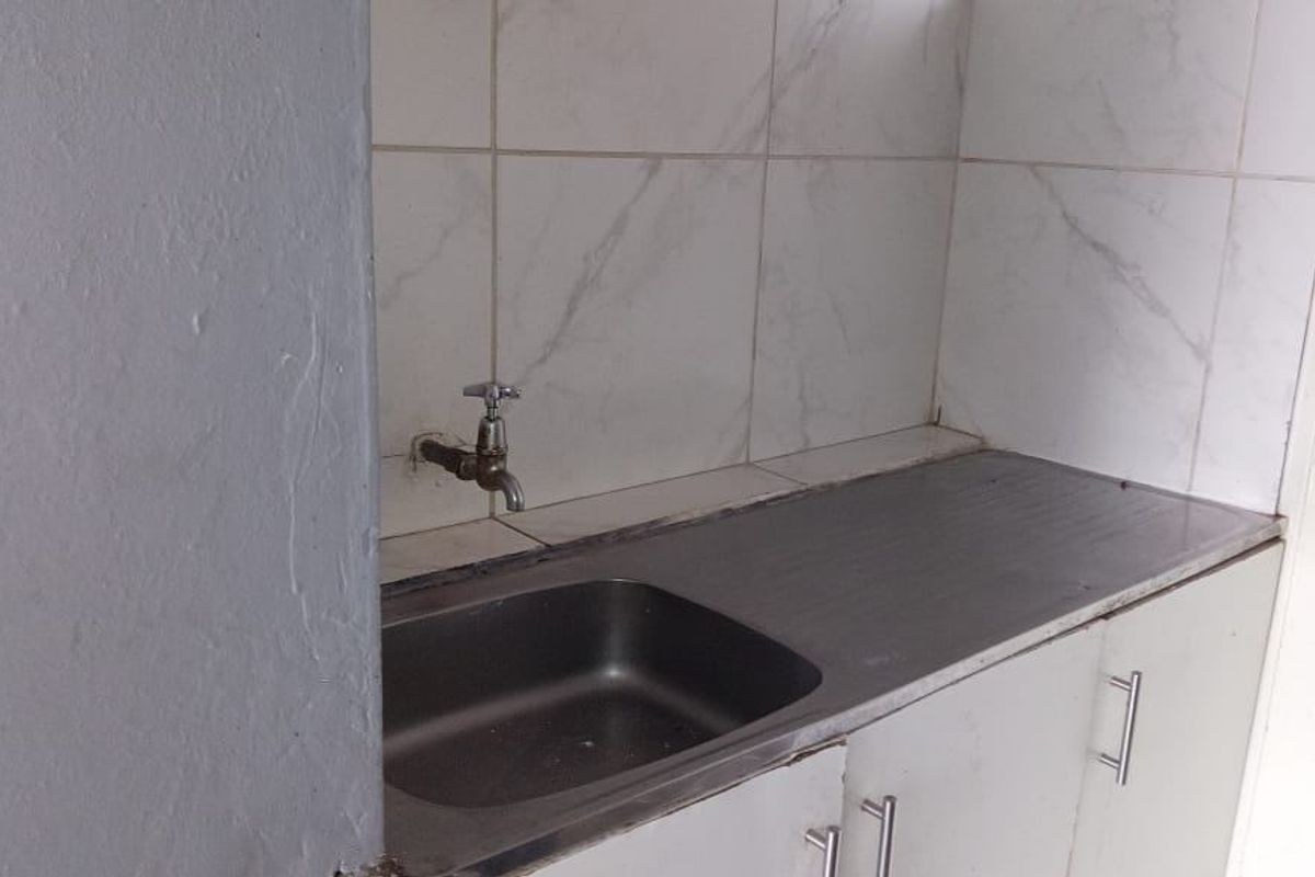 A functional laundry area featuring a stainless steel sink, built-in cabinetry, and marble-look wall tiling.