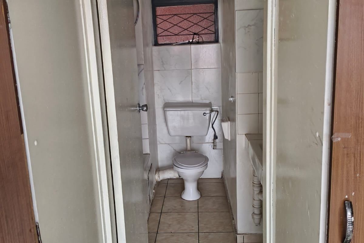 A compact, dated bathroom featuring tiled flooring, wall tiles, a pedestal basin, and a toilet, requiring cosmetic updates to modernize the space.