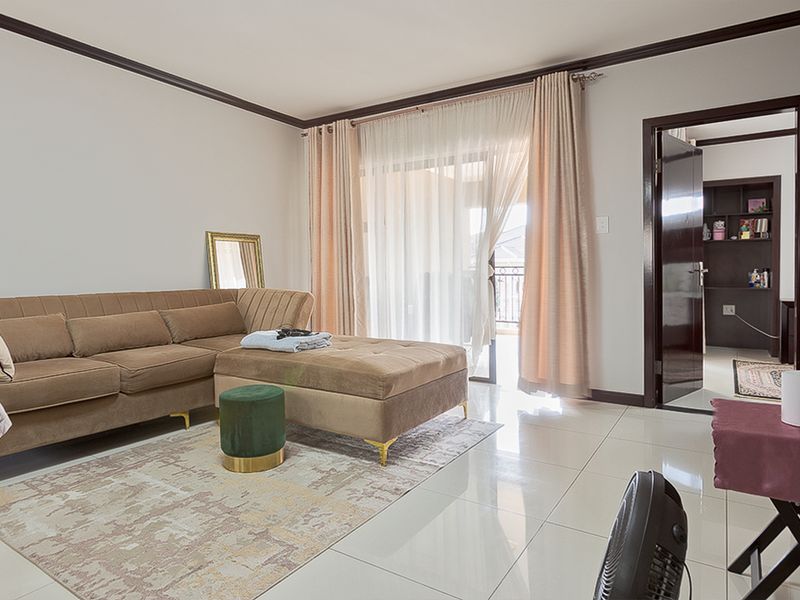 A bright living room featuring polished tile flooring, crown molding, and a sliding glass door providing access to an outdoor balcony area.