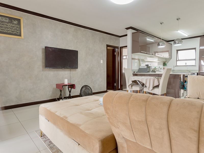 Open-plan living and kitchen area featuring modern glossy cabinetry, stone countertops, tiled flooring, and elegant crown molding throughout the space.