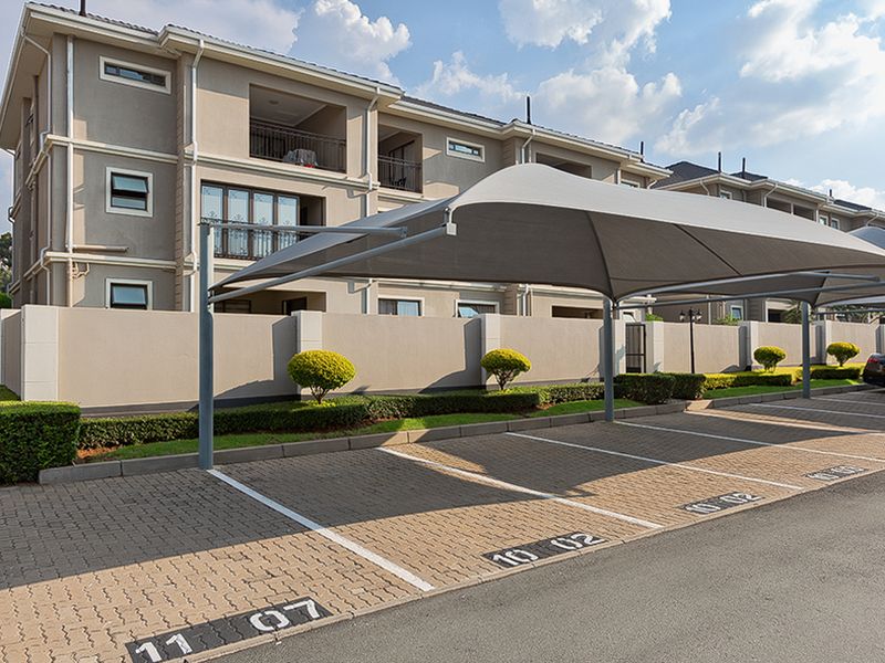 Exterior view of the apartment complex featuring designated paved parking bays with shade cloth carports and well-maintained perimeter boundary walls.