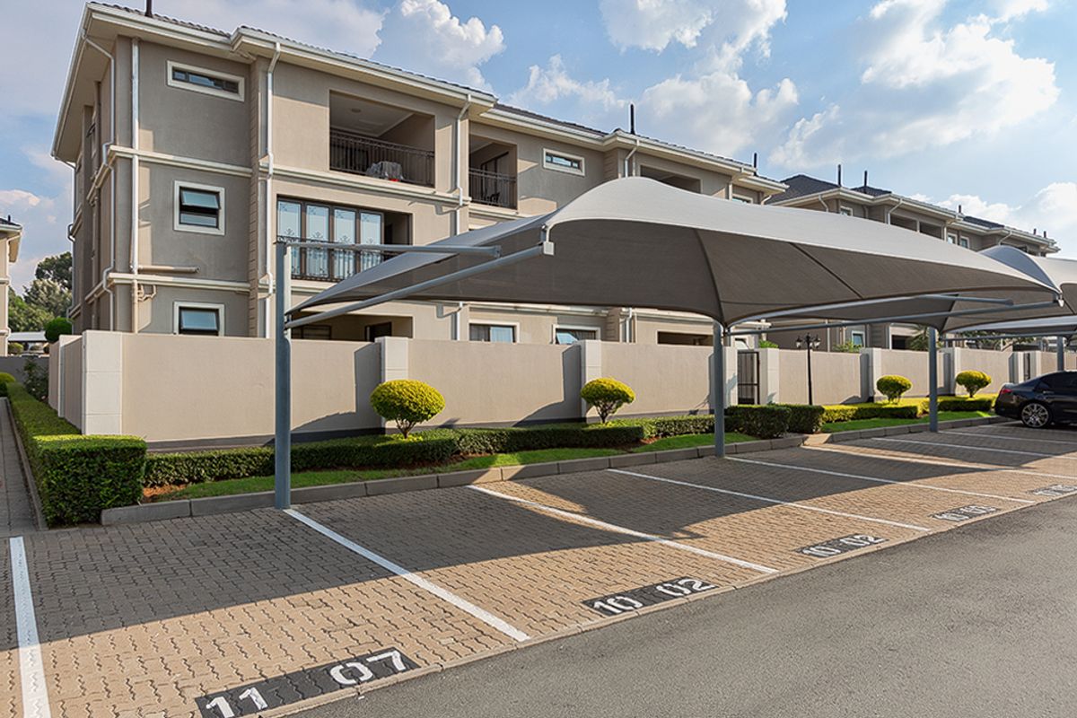 Exterior view of the apartment complex featuring designated paved parking bays with shade cloth carports and well-maintained perimeter boundary walls.