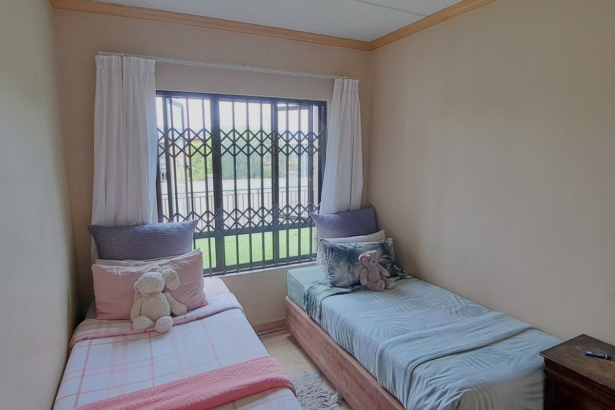 A compact bedroom featuring laminate flooring, neutral wall finishes, and a window fitted with a security gate.
