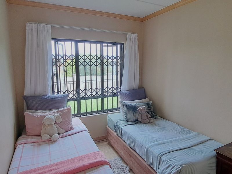 A compact bedroom featuring laminate flooring, neutral wall finishes, and a window fitted with a security gate.