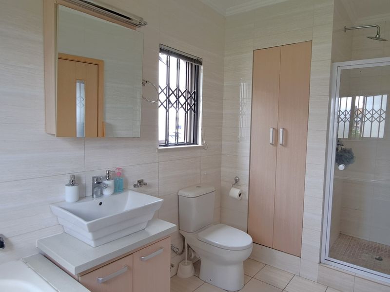 A modern bathroom featuring a vessel sink vanity, a separate shower enclosure, a toilet, and built-in storage cabinetry with neutral wall tiling.