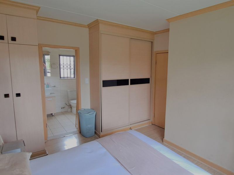Bedroom featuring built-in cupboards, laminate flooring, and an adjoining en-suite bathroom with tiled finishes.