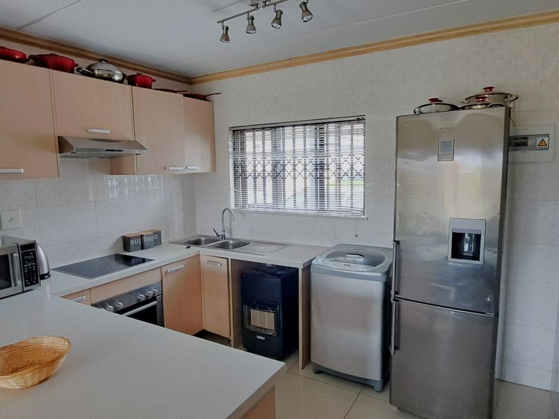 Functional kitchen featuring light wood-tone cabinetry, laminate countertops, tiled splashbacks, and integrated appliances, offering a practical layout for daily meal preparation.