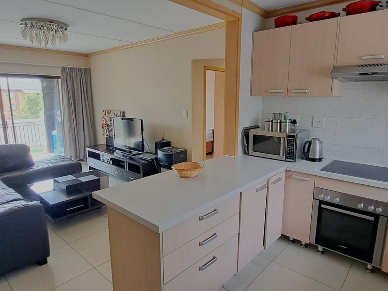 Open-plan living and kitchen area featuring light wood cabinetry, built-in oven and hob, tiled floors, and access to a balcony through sliding glass doors.