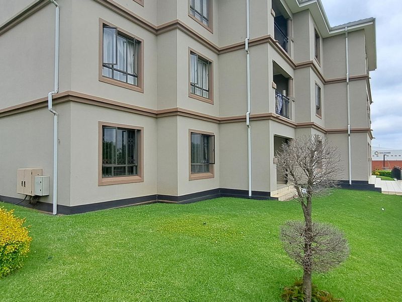 A view of the rear facade of a multi-story apartment building featuring well-maintained lawns and landscaped garden areas.