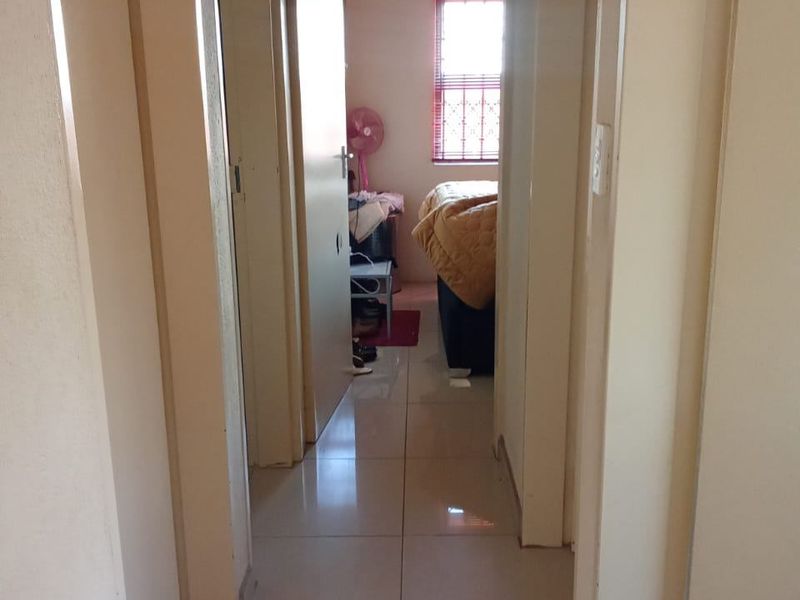 A functional hallway with tiled flooring providing access to adjacent rooms, including a bedroom visible at the end of the corridor.