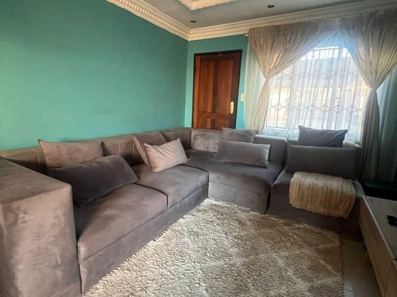 A living room featuring decorative ceiling molding, a central ceiling rose, tiled flooring, and a window fitted with a security gate.