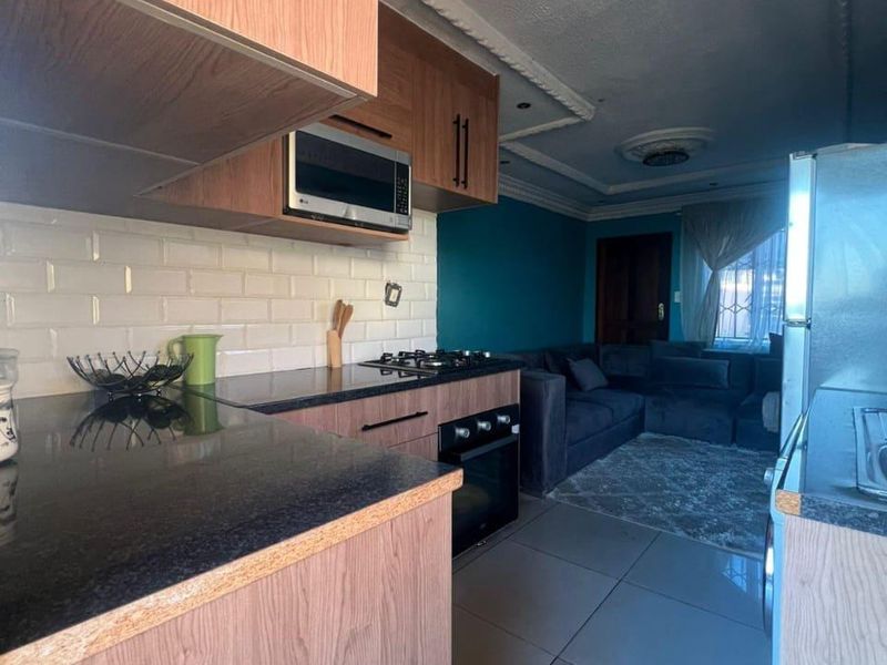 Open-plan kitchen and living area featuring wood-finish cabinetry, granite countertops, subway tile backsplash, and decorative ceiling cornices.