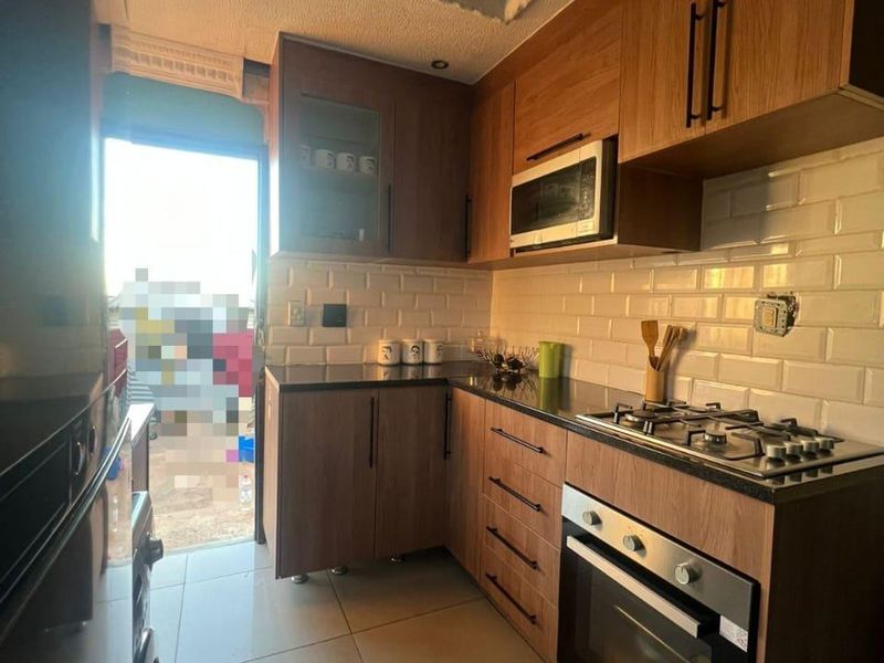 A compact kitchen featuring wood-finish cabinetry, subway tile backsplash, stone countertops, and integrated appliances, with direct access to an outdoor area.