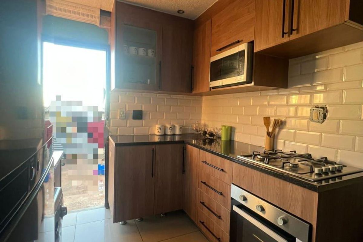 A compact kitchen featuring wood-finish cabinetry, subway tile backsplash, stone countertops, and integrated appliances, with direct access to an outdoor area.