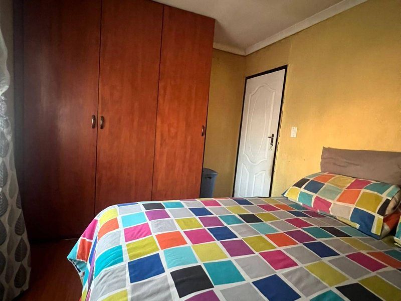A functional bedroom featuring a large built-in wooden wardrobe, laminate flooring, and a coved ceiling, offering a practical layout for a comfortable sleeping space.