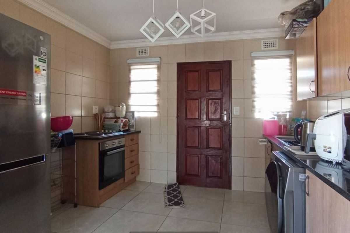 A functional kitchen featuring tiled walls and floors, built-in cabinetry, an integrated oven and hob, and natural light through dual windows.