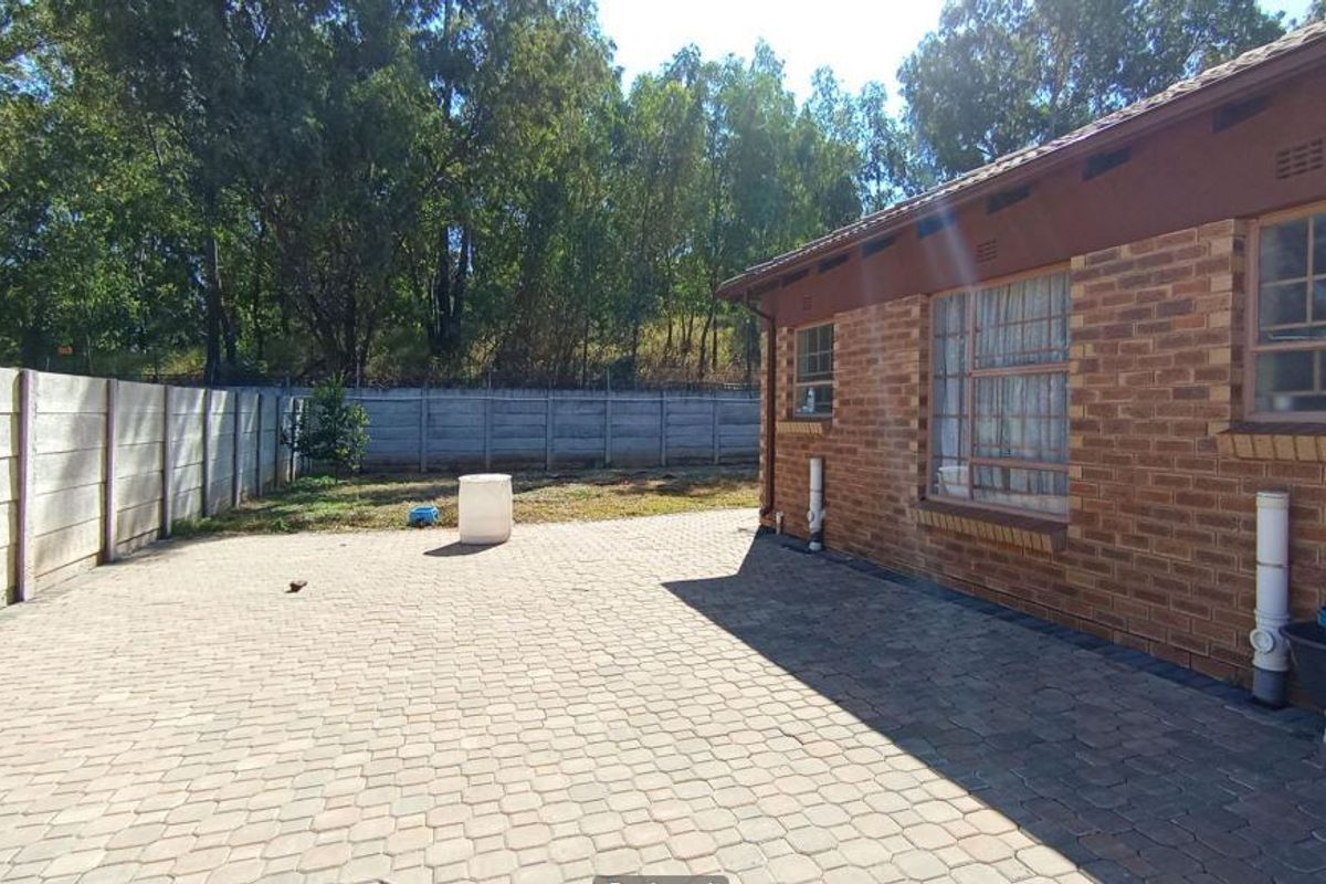 Rear exterior view featuring a paved patio area, brick facade, and a secure precast concrete boundary wall.