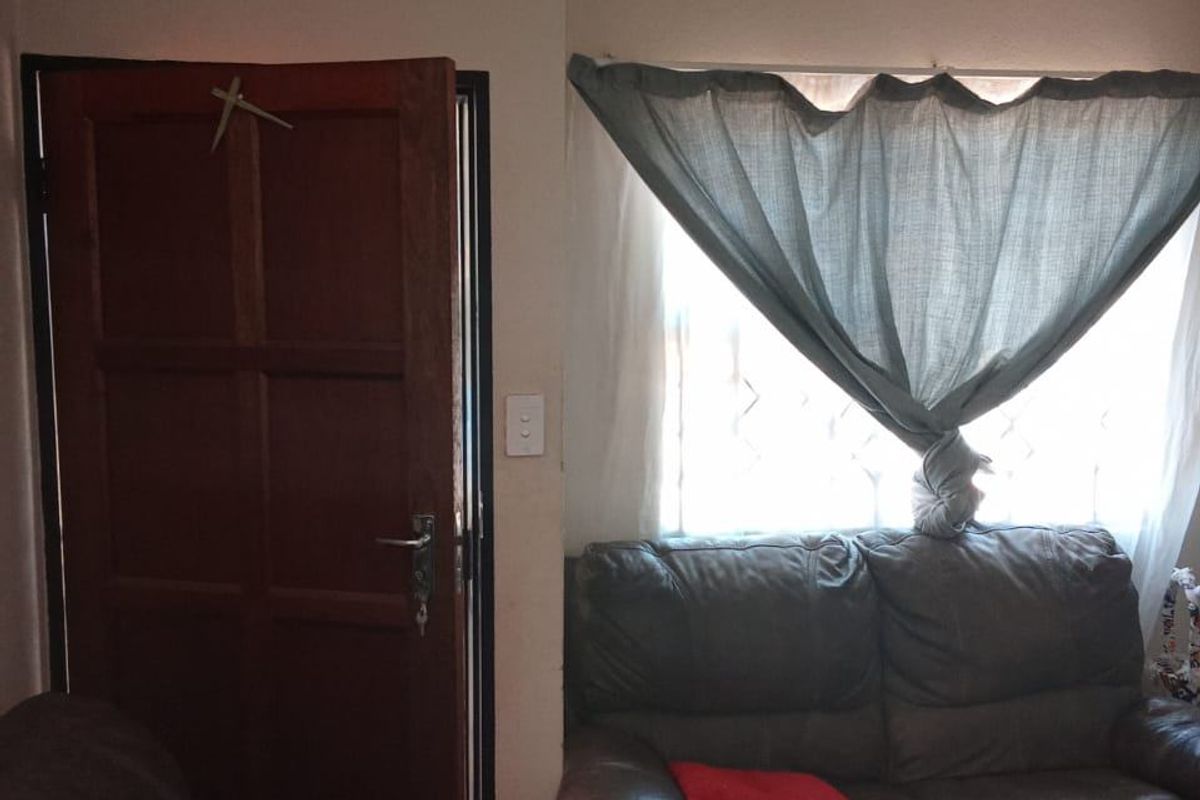 A living room area featuring a timber panel door, security gate, and a window fitted with burglar bars.
