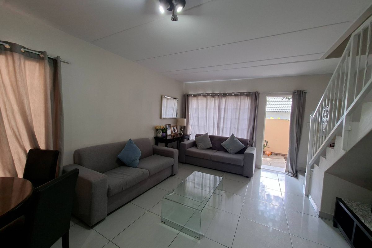 A bright living room featuring tiled flooring, a staircase with a metal balustrade, and direct access to an outdoor patio area through a sliding door.