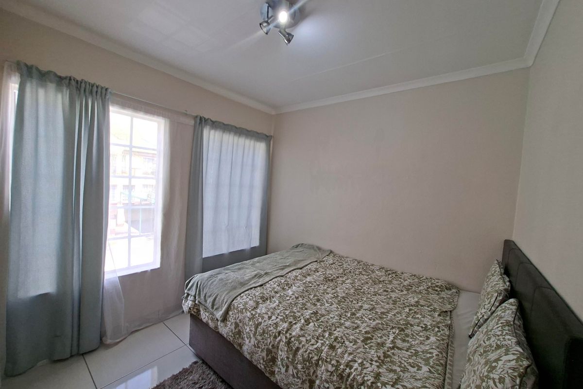 A functional bedroom featuring tiled flooring, a ceiling-mounted spotlight fixture, and windows with muntins, providing natural light.